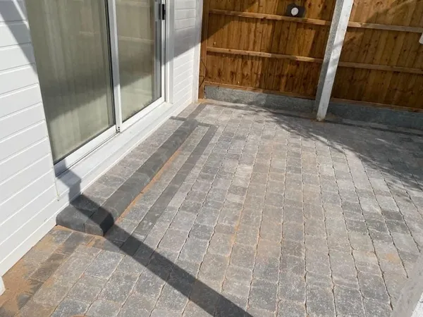 Grey tumbled block paving patio with two block steps up to a sliding door