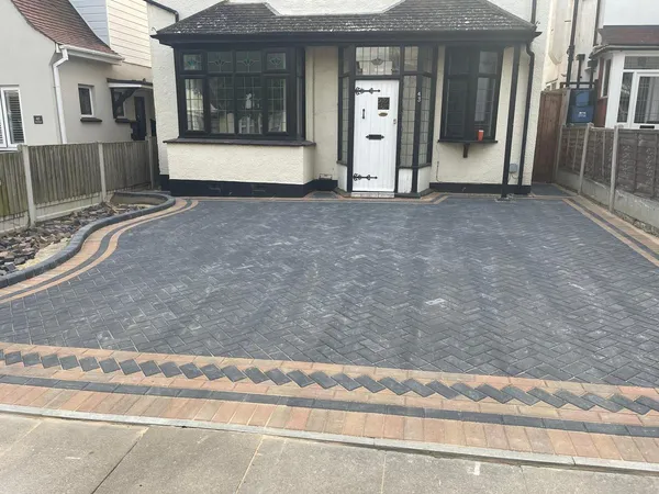 Charcoal herringbone block paving driveway with a buff double border and chevron inlay in front of a 1930s detached house