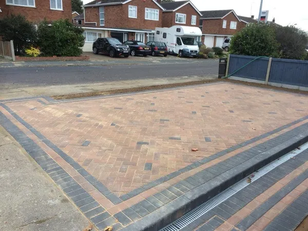 Buff and brindle herringbone block paving with a charcoal double border and a drainage channel at the threshold