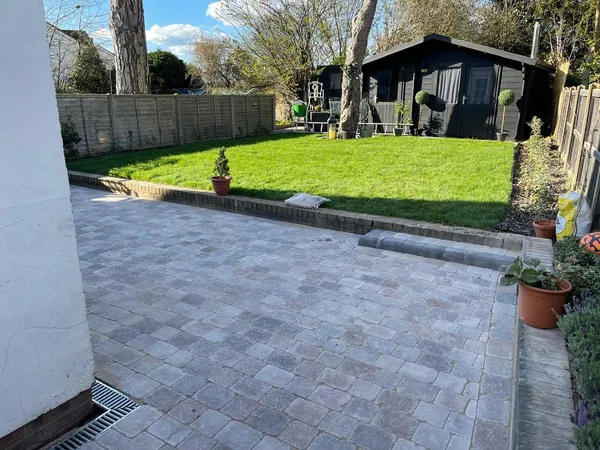 Grey tumbled block paving patio with a raised kerb edge, lawn and summerhouse behind