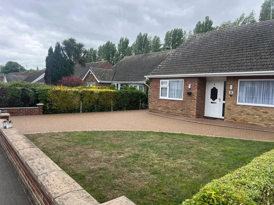 Golden resin bound driveway at a bungalow with a brick wall and lawn, laid by First4Driveways