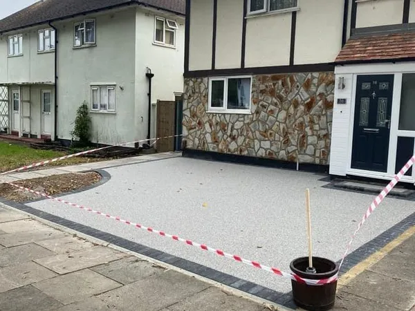 Newly laid pale silver resin bound driveway with a charcoal block border in front of a mock-Tudor semi with stone cladding